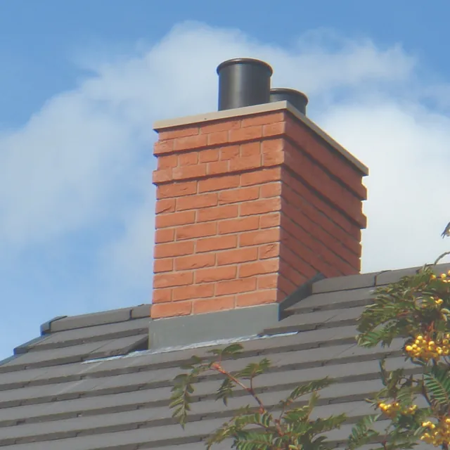 Red brick chimney stack with two pots and lead flashing on a tiled ridge