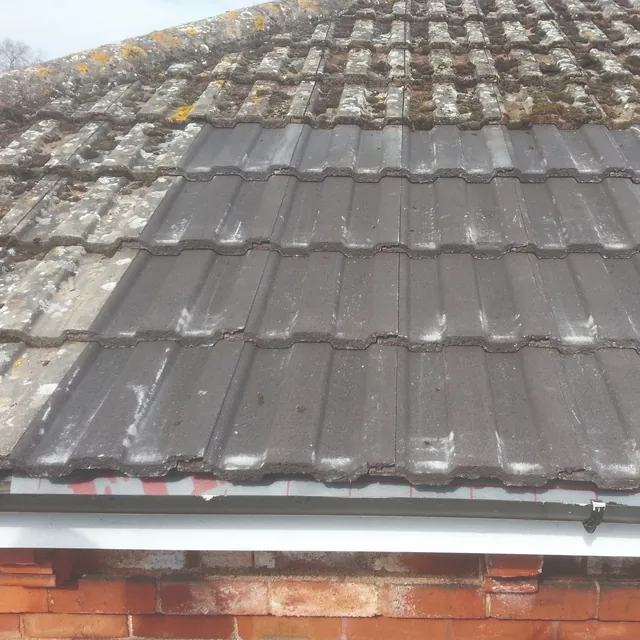 New grey concrete tiles patched into an older lichen-covered roof at the eaves